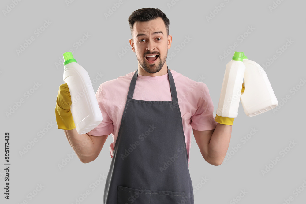 Male janitor with bottles of detergent on grey background Male janitor with bottles of detergent on grey background