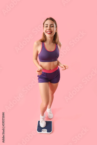 Sporty young woman measuring her weight on scales against pink background © Pixel-Shot