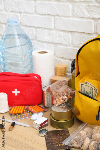 Necessities for emergency bag on wooden table near white brick wall © Pixel-Shot