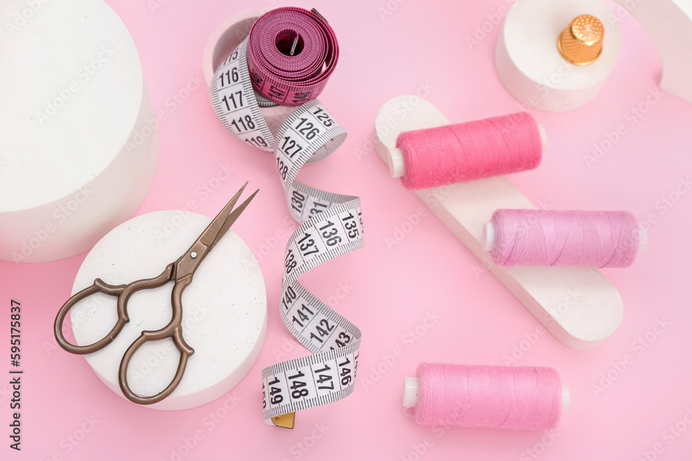 Podiums with scissors, thread spools and measuring tapes on pink background Podiums with scissors, thread spools and measuring tapes on pink background