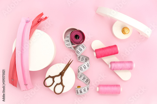 Podiums with scissors, thread spools, measuring tapes and zips on pink background