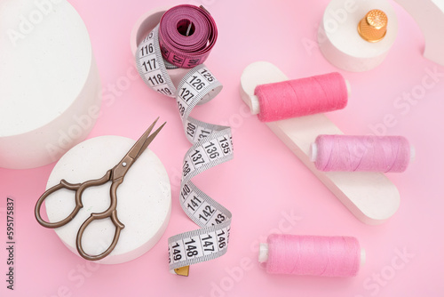 Podiums with scissors, thread spools and measuring tapes on pink background