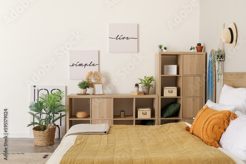 Interior of light bedroom with houseplants and shelving unit