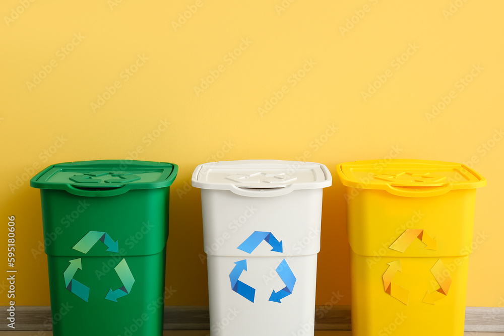 Different garbage bins with recycling symbol near yellow wall Different garbage bins with recycling symbol near yellow wall