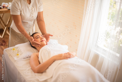 Professional masseuse is massaging her scalp and temples with gentle circular motions in spa room.