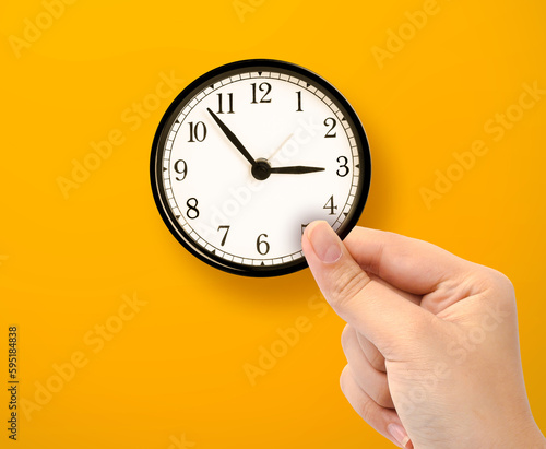 Hand holding small clock on yellow background
