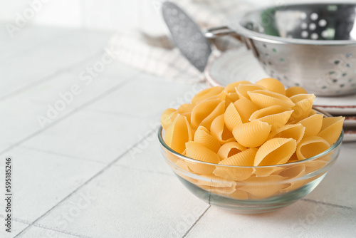 Bowl with raw conchiglie pasta on white tile background photo