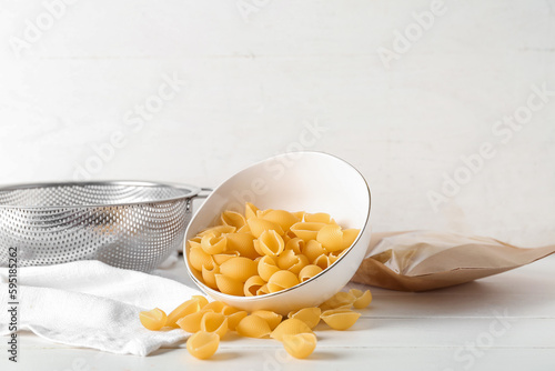 Bowl with raw conchiglie pasta on light wooden background photo