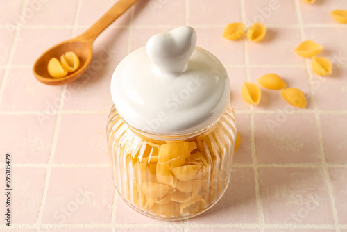 Jar with raw conchiglie pasta on pink tile background photo