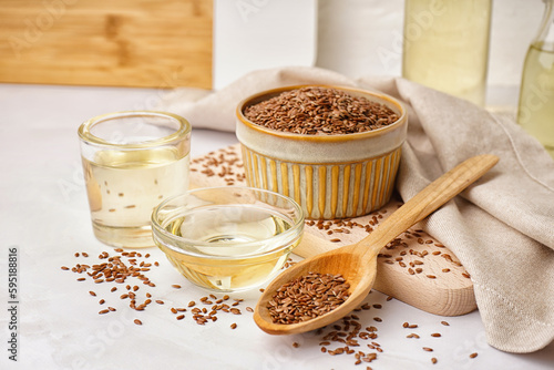 Bowl, glass with flax oil and spoon of seeds on white background