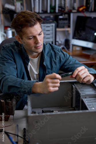 Young caucasian man disassembles broken computer. Computer service and repair concept. Computer disassembling in repair shop, workshop. Electronic development by professional technician