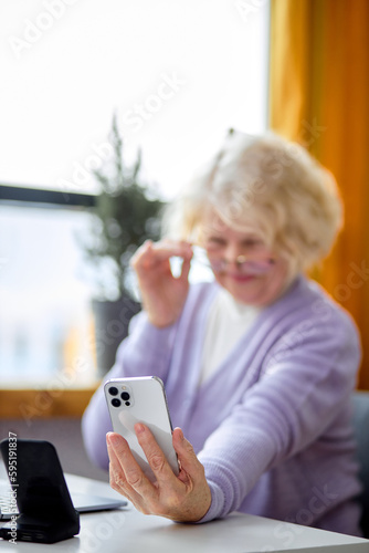 Pretty elderly caucasian woman checking emails and reading messages on smartphone, at home. Happy aged senior grandmother using modern mobile phone alone, focus on smartphone in hands