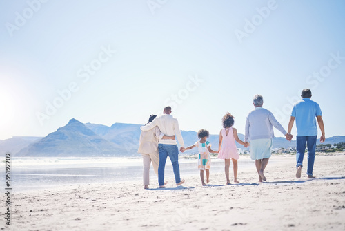 Holding hands, back and big family at the beach for walking, holiday and summer weekend by the ocean. Affection, support and parents, children and grandparents on a walk by the seaside for bonding