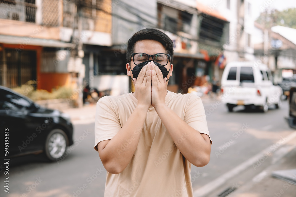 Fototapeta premium Asian young man wearing face mask to protect PM 2.5, protect pollution, anti smog and viruses on road in the city. Global warming concept. Healthcare concept. Environmental pollution concept.