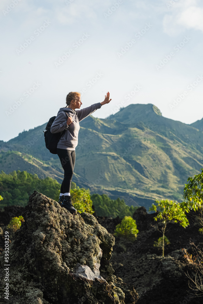 A young girl traveler with a backpack walks in the mountains against the backdrop of the Batur volcano on the island of Bali in Indonesia.