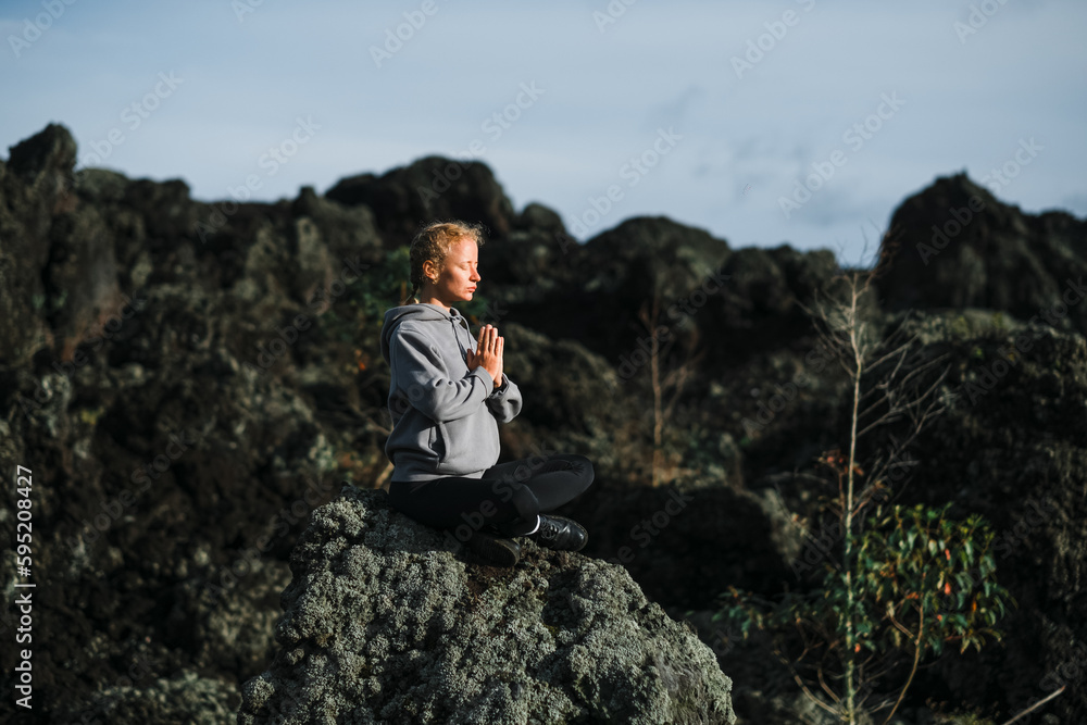 A young beautiful girl, a yogini, sits in the mountains, with her eyes closed, clasped her hands in namaste and meditates.