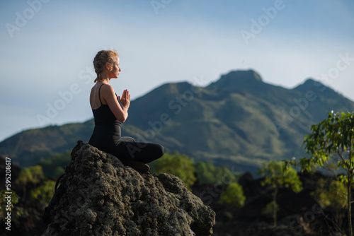 A young beautiful girl, a yogini, sits in the mountains, with her eyes closed, clasped her hands in namaste and meditates. © Evgenii