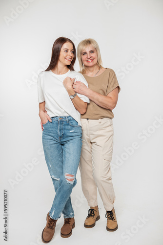 Beautiful happy girl woman and elderly smiling mother in fashionable casual clothes on a white background, full length portrait
