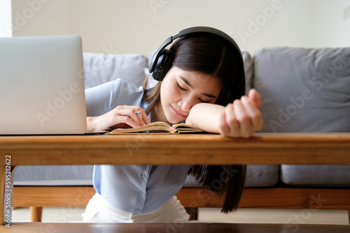 Pretty young asian woman wearing headphone fall asleep distracted from work, sleeping at working desk