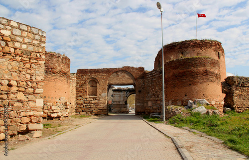 A view of one of the gates with round towers and a wall surrounding the historic part of Iznik against a blue cloudy sky photo