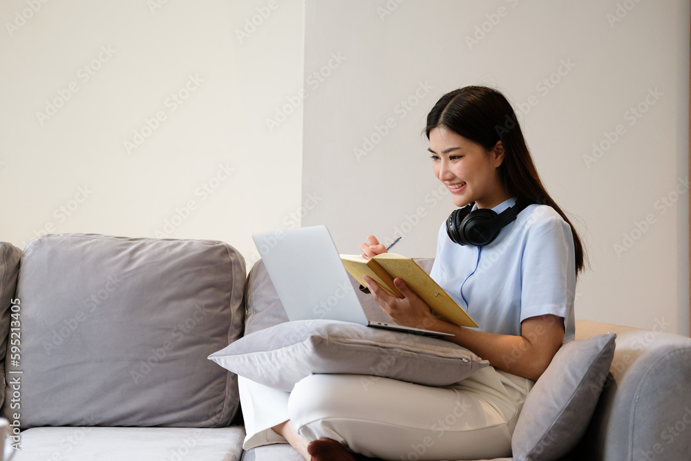 Concept of activity in living room, Young Asian woman is taking notes while learning lesson online Concept of activity in living room, Young Asian woman is taking notes while learning lesson online