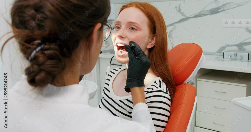 redhead woman sits with opened mouth gets dental treatment at dental