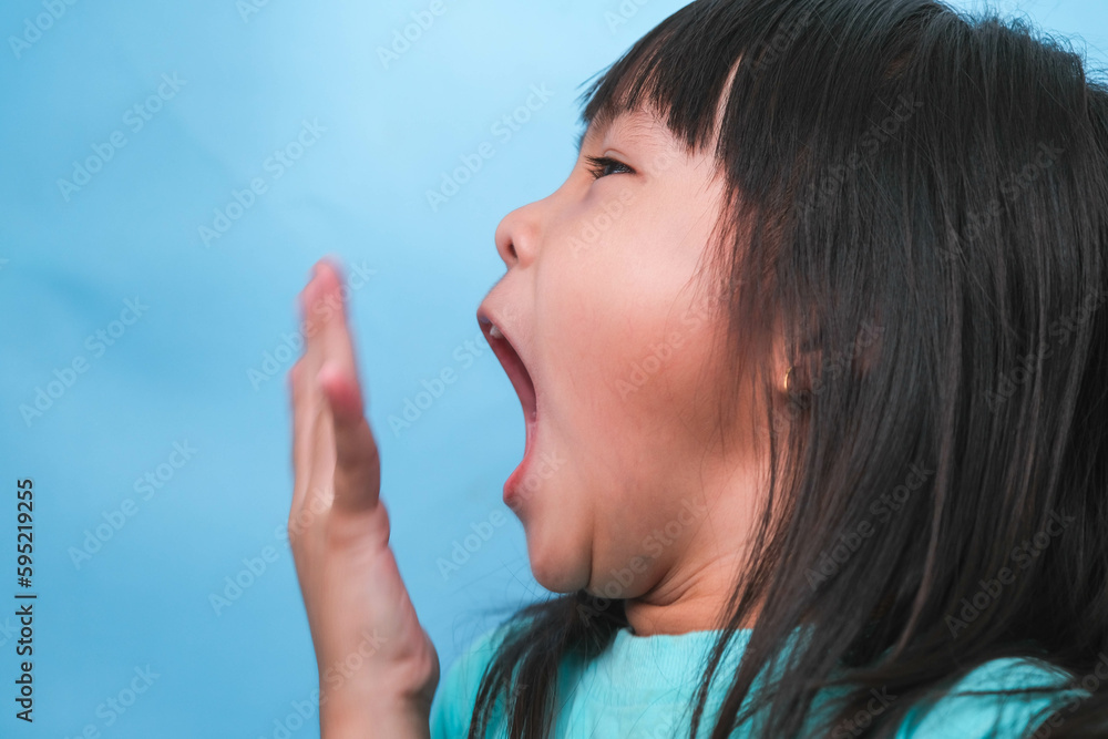 Little asian girl covering her mouth to smell the bad breath. Child girl checking breath with her hands. Oral health problems or dental care concept. Little asian girl covering her mouth to smell the bad breath. Child girl checking breath with her hands. Oral health problems or dental care concept.