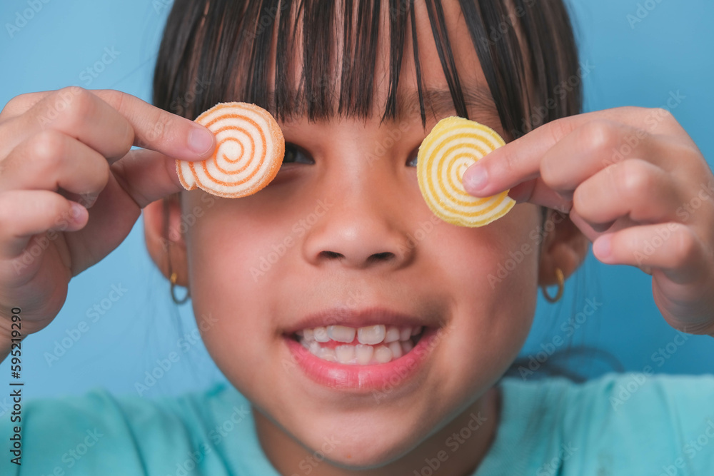 Smiling cute little girl covering her eyes with two gelatinous sweets