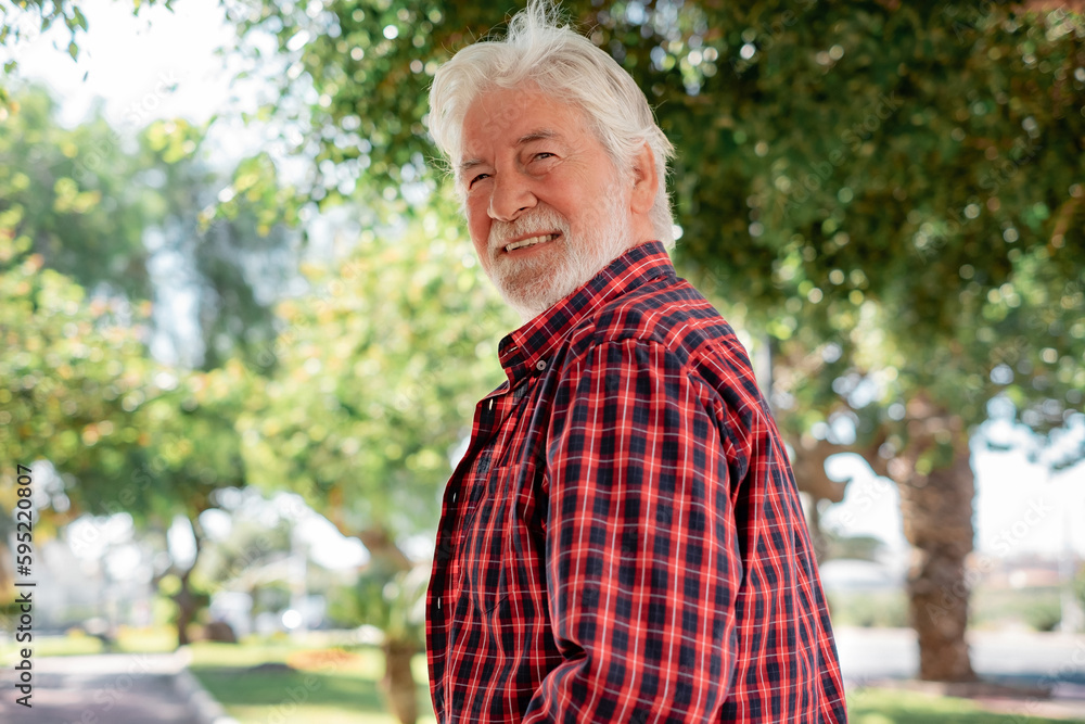 Portrait of handsome senior white-haired man walking in the city park looking at camera smiling Portrait of handsome senior white-haired man walking in the city park looking at camera smiling
