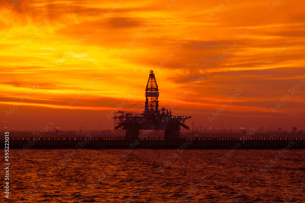 Offshore oil rig moored to the port pier at red sunset at dusk.