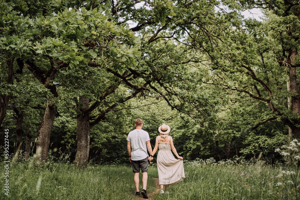 Couple Walking In The Park Trail Between Beautiful Oak Trees With Green Leaves Holding Hands In Summer