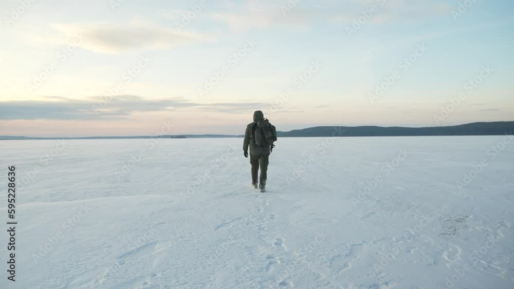 The man with the backpack goes far along the frozen lake covered with snow. Winter landscape The man with the backpack goes far along the frozen lake covered with snow. Winter landscape