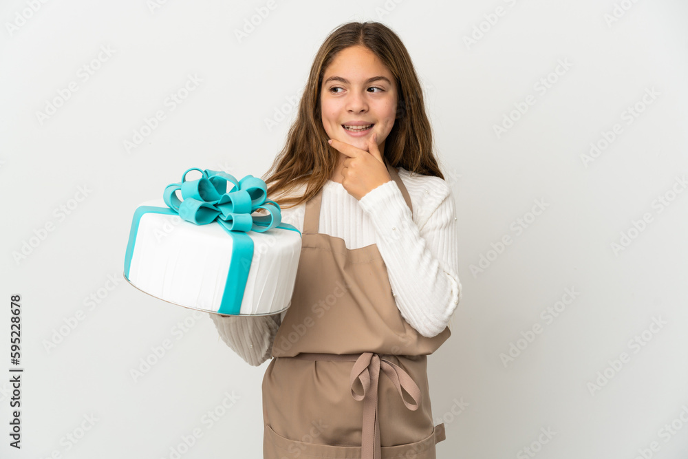 Little girl holding a big cake over isolated white background looking to the side and smiling Little girl holding a big cake over isolated white background looking to the side and smiling