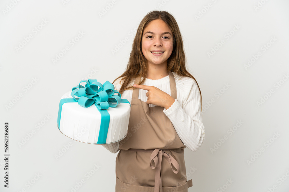 Little girl holding a big cake over isolated white background pointing to the side to present a product Little girl holding a big cake over isolated white background pointing to the side to present a product