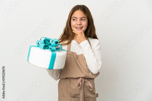 Little girl holding a big cake over isolated white background looking to the side and smiling