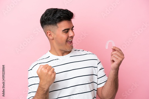Young caucasian man holding invisaling isolated on pink background celebrating a victory photo