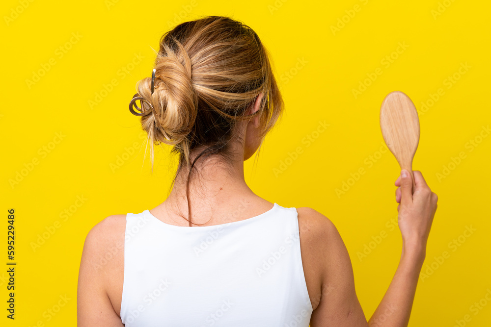 Young Uruguayan woman with hair comb isolated on yellow background in back position Young Uruguayan woman with hair comb isolated on yellow background in back position