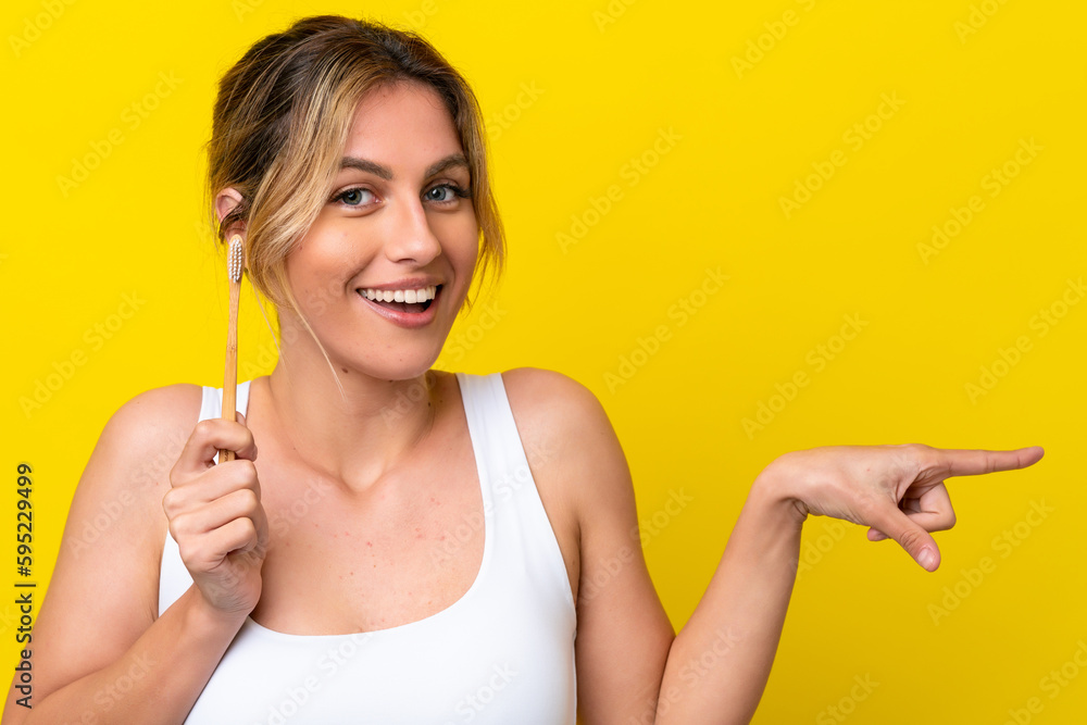 Young Uruguayan woman brushing teeth isolated on yellow background surprised and pointing finger to the side Young Uruguayan woman brushing teeth isolated on yellow background surprised and pointing finger to the side