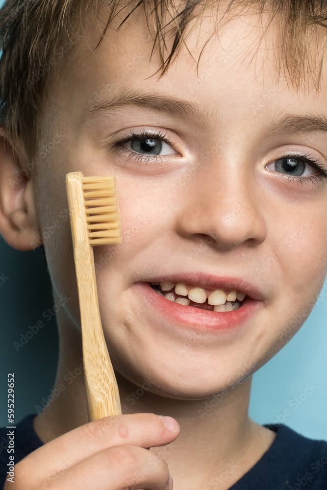 a boy of European appearance holds a bamboo toothbrush near his face. eco-friendly a boy of European appearance holds a bamboo toothbrush near his face. eco-friendly