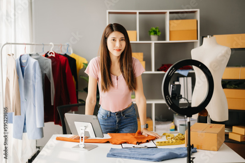 Fashion blogger concept, Young Asian women selling clothes on video streaming.Startup small business SME, using smartphone or tablet taking receive and checking.