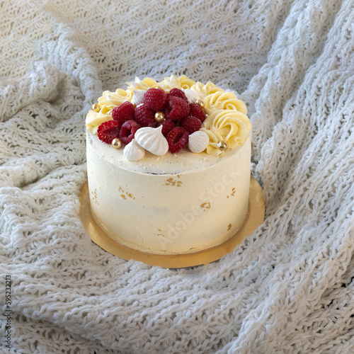 Gold & white birthday cake topped with raspberrys and meringue. 