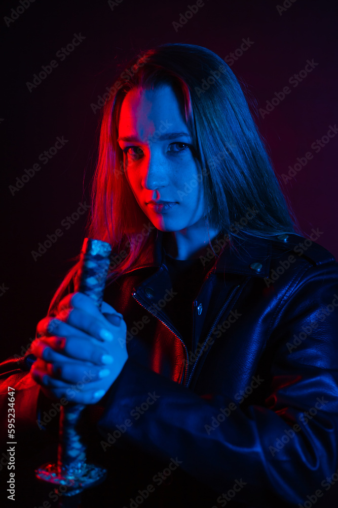A young beautiful woman with long hair in a black leather jacket holds a katana at night in the dark. Robber in the city in neon blue and red light with melee weapons. A young beautiful woman with long hair in a black leather jacket holds a katana at night in the dark. Robber in the city in neon blue and red light with melee weapons.