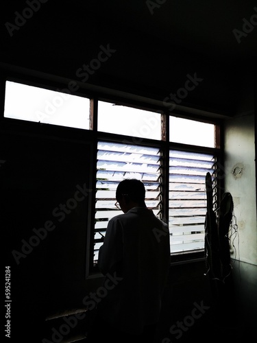Turn back, Asian young man stands near window in the old building and looking at screen, reading message on his mobile phone, Take a break from work.