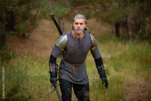 an old warrior in chain mail with a sword is looking for prey in the forest.