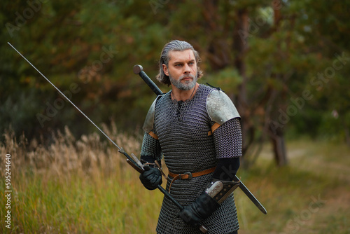 an old warrior in chain mail with a sword is looking for prey in the forest.