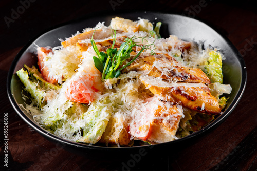 Caesar salad with croutons, cheese, eggs, tomatoes and grilled chicken on black wooden table