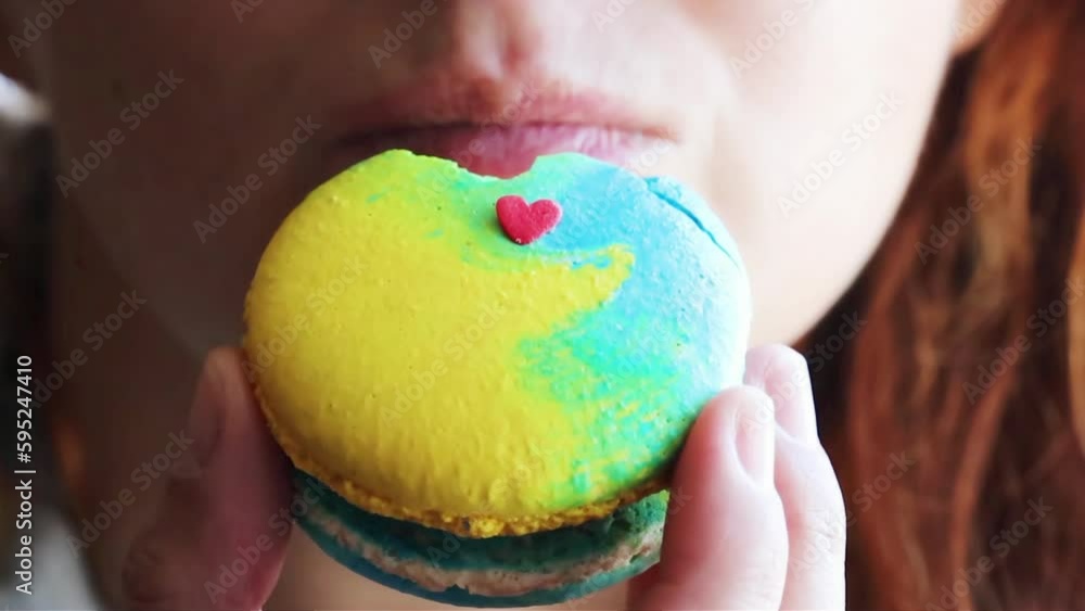 Young girl eating macaroon cake bleu and yellow color with small red heart on it Young girl eating macaroon cake bleu and yellow color with small red heart on it
