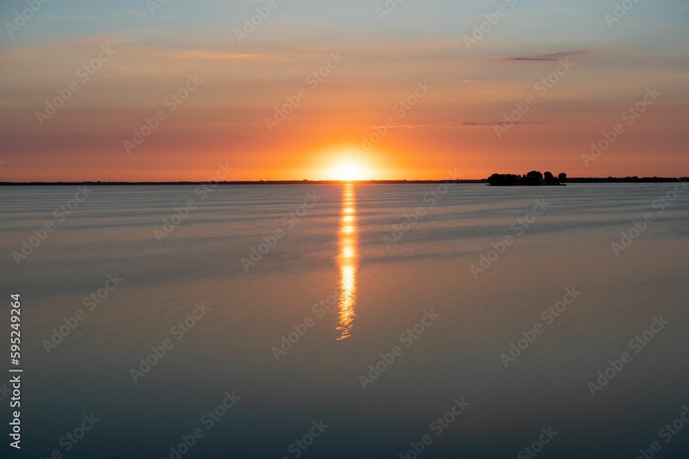 Beautiful, tranquil scene of a vibrant orange sunset reflecting off of the water