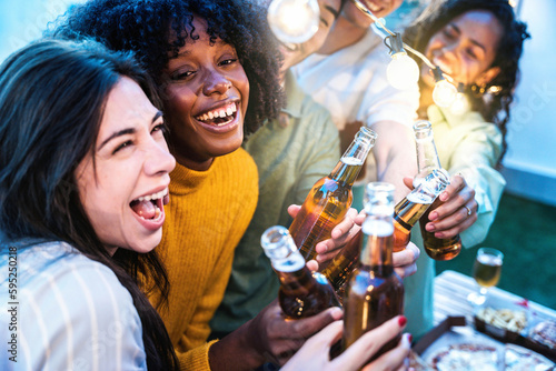 Happy friends enjoying party on rooftop terrace - Group of multiracial young people drinking beer bottle at brewery pub garden - Life style concept with guys and girls hanging outdoors