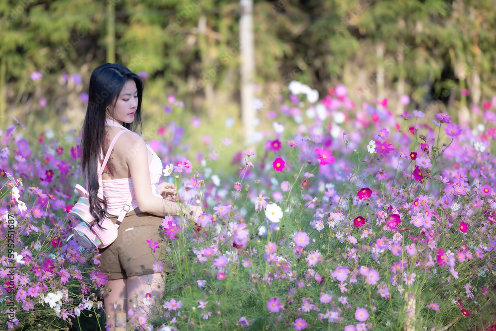 Beautiful woman happy traveler walking in the flowers garden. Young woman smile and relaxing with happy around outdoor garden. Woman's hand touching and enjoying beauty cosmos flowers.Travel concept. Beautiful woman happy traveler walking in the flowers garden. Young woman smile and relaxing with happy around outdoor garden. Woman's hand touching and enjoying beauty cosmos flowers.Travel concept.